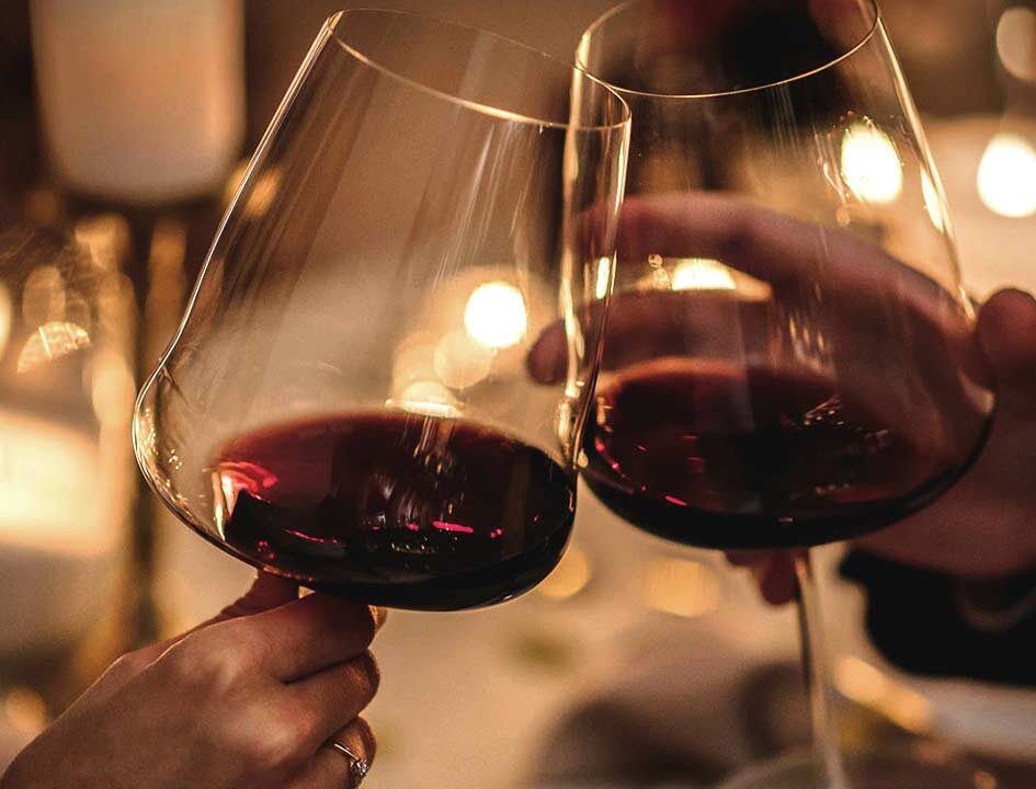 Due calici di vino rosso che si toccano per un brindisi romantico, con un'atmosfera intima e candele accese sullo sfondo.